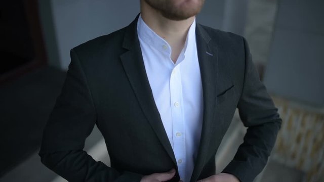 Man in custom tailored suit posing outdoors and buttoning his jacket.