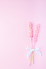 Rock candy on pink paper background decorated with a white bow, vertical, top view, copy space
