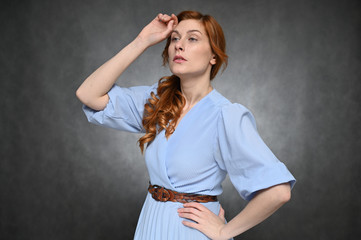 Girl Model posing in the studio on a gray background. Portrait of a pretty red-haired young woman in a blue blouse.