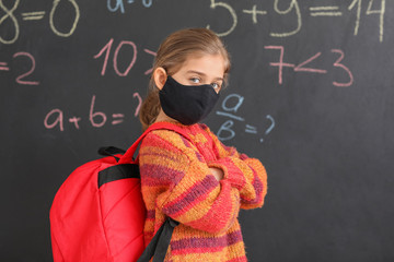 Little girl wearing medical mask near school blackboard
