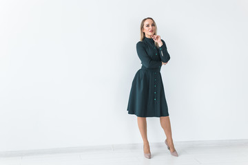 Fashionable young blonde woman in beautiful elegant dress posing at white studio with copy space.