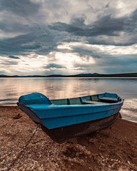 The blue boat moored to the lake under stormy clouds