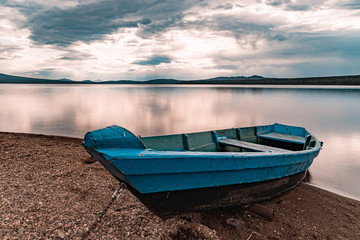 The blue boat moored to the lake under stormy clouds