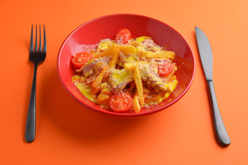 Melting cheddar cheese over the top of french fries covered in spicy sauce with meat and tomatoes. Orange background.