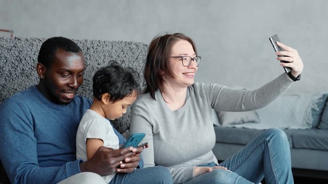 Happy mixed ethnicity family little african dad kid son and caucasian mom holding phone having fun with smartphone, mother father with child boy looking at cellphone enjoy using mobile apps at home
