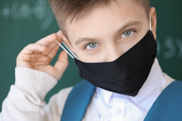 Little schoolboy wearing protective mask in classroom. Concept of epidemic