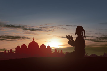 Silhouette of Muslim man sitting while raised hands and praying