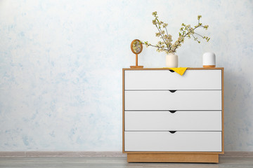 Vase with beautiful blooming branches on chest of drawers in room