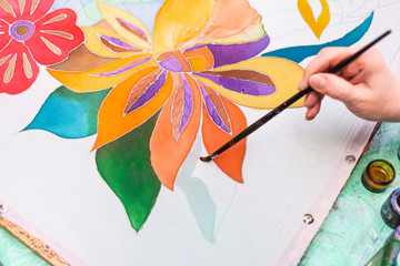 master-class of batik coloring - painter draws floral pattern on white silk canvas on wooden frame in cold contour batik technique
