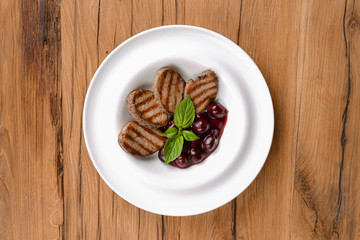 Grilled meat pieces with berry sauce served on a white plate over dark rustic wooden background. Italian cuisine.