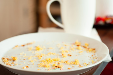 An empty round white plate with the remains of baking crumbs is standing near a white cup.