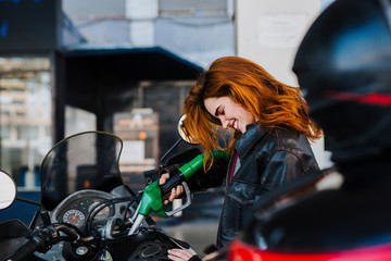 Fototapeta na wymiar young woman refueling her motorcycle at the gas station, concept of refueling and traveling