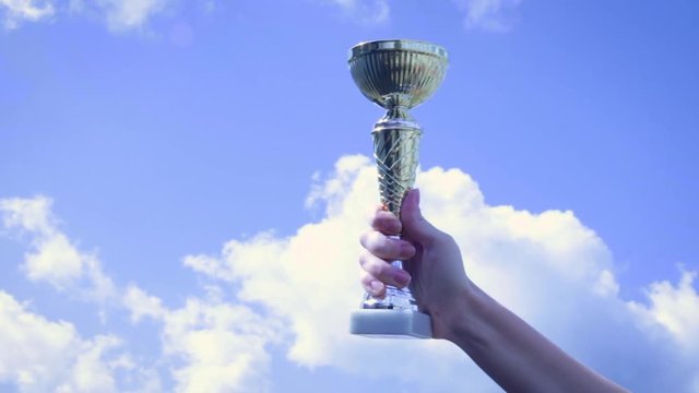 A woman holding up a trophy cup as a winner in a competition against the sky with clouds. First place. Concept as victory, success and champion in sport.