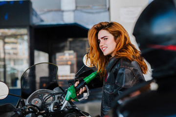 Plakat young woman refueling her motorcycle at the gas station, concept of refueling and traveling