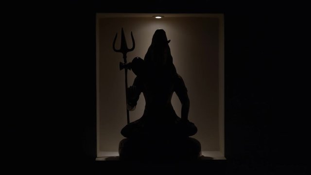 Lights reveal Lord Shiva statue in alcove in darkness