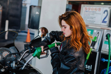 young woman refueling her motorcycle at the gas station, concept of refueling and traveling