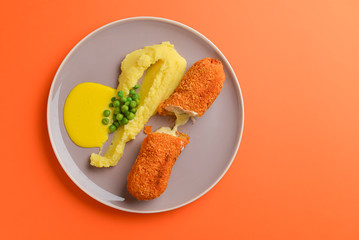 Cordon bleu cutlet, deep fried meat served with mashed potatoes and green peas on gray plate over orange background.