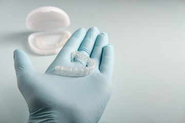 The doctor in gloves holds in his hand a plastic mouthpiece for teeth, on a blue background, a...