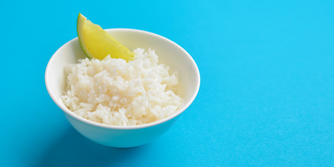 White rice with a piece of lime served in a small white bowl. Isolated on bright blue background.
