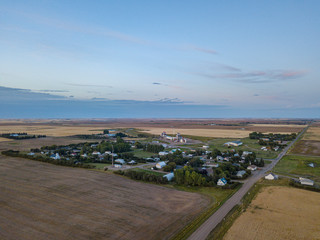 Drone footage aerial of village in the middle of fields nowhere in Canada Saskatchewan between roads and fields during sunset with blue sky and clouds 