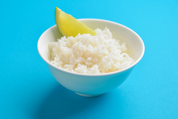 White rice with a piece of lime served in a small white bowl. Isolated on bright blue background.