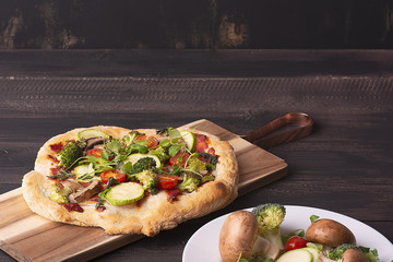 Vegetarian pinsa with vegetables on Roman pastry with broccoli, zucchini, tomatoes, mushrooms, microgreens. No cheese. Copy space. on a dark wooden background. rustic. Recipe