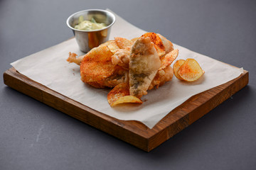 British Traditional Fish and chips with tartar sauce on crumpled paper served on wooden cutting board