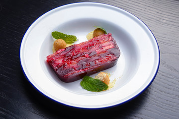 Red and pink layers of gelatin dessert served on a white plate over black wooden table.