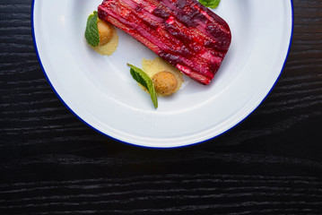 Red and pink layers of gelatin dessert served on a white plate over black wooden table.