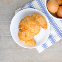 Croissant on white plate and raw chicken eggs on wooden rustic background. the view from the top