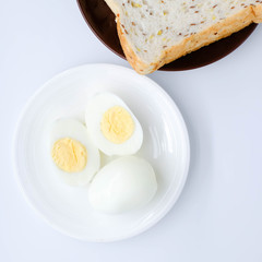 halves of boiled eggs on white plate and sliced loaf of sprouted grain and seed bread on white background. the view from the top
