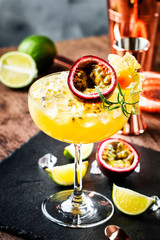 Alcoholic cocktail with fresh passion fruit with rosemary and ice. Gray wood background, bar tools, copy space
