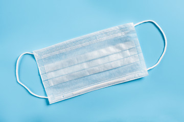 Disposable surgical mask on a blue background. Typical 3-ply surgical mask to cover the mouth and nose.