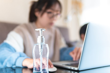 Empty bottle of hand sanitizer alcoholic gel at home office. Young freelance woman working at home while taking care of kids. Remote work during coronavirus pandemic