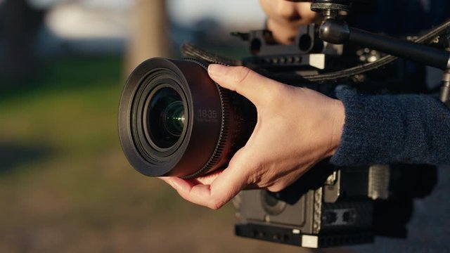 Female filmmaker shifts focus on cinema camera with cine lens in golden sunset