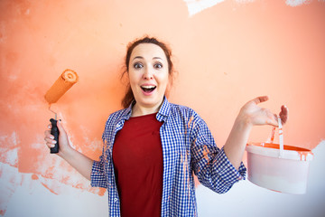 Funny young woman painting interior wall with paint roller in new house. A woman with roller applying paint on a wall.