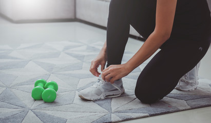 Woman getting ready for workout at home. She is tying shoelace on sneakers.Sport and recreation...