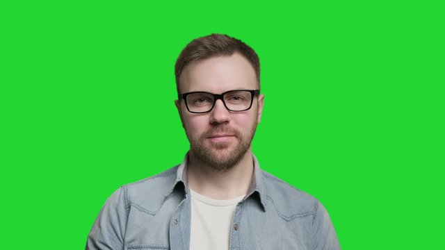 Handsome caucasian man with beard putting on glasses and looking at camera. Isolated shot at green screen. Portrait of cheerful guy in 4K, UHD