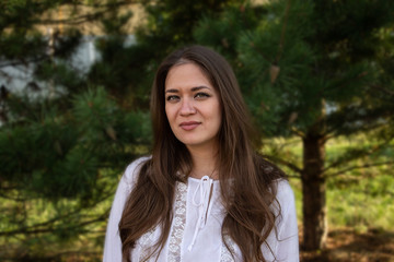Naklejka premium Portrait of a young brown-haired beautiful girl with green eyes and a white blouse on a background of trees