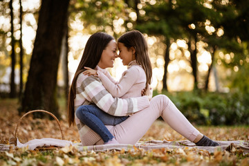 Mother and daughter enjoying autumn in park. They are embracing.