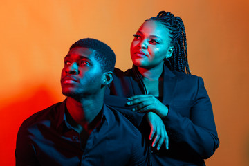 Portrait of young african american couple in love posing at studio dressed in classic clothes. Neon...
