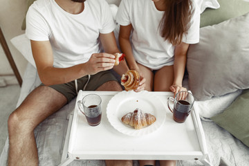Cute couple in a bedroom. Lady in a white t-shirt. Man brought breakfast to bed.