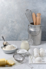 Fototapeta na wymiar in the kitchen on the gray textured background, some utensils, flour, milk and eggs and various ingredients ready for the preparation of homemade culinary recipes