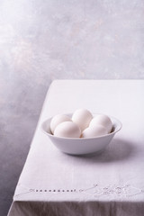 on the white linen tablecloth, in the foreground, a ceramic bowl with fresh white eggs ready for the preparation of homemade culinary recipes