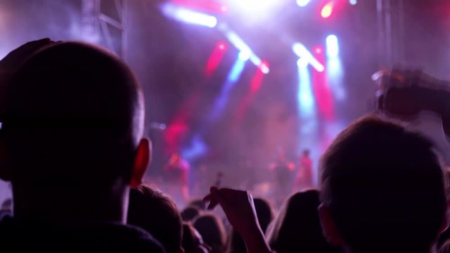 Happy people are watching an amazing musical concert. Merry fans jump and raise their hands up. Crowd of excited fans applauding to popular band performing favorite song. The crowd watches a concert.