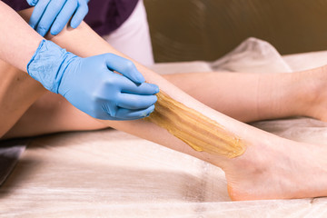 Woman having hair removal procedure on leg with sugaring paste in salon, close-up. Cosmetology...