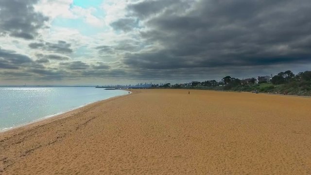 Aerial footage of empty vast orange sand beach with and city in the background on a cloudy weather afternoon at Brighton Beach, Melbourne, Victoria, Australia.