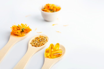Herbal capsule, natural vitamins, dry calendula flowers at wooden spoon on white background. Concept of healthcare and alternative medicine: homeopathy and naturopathy. Close up, copy space for text