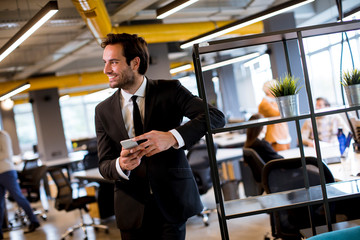 Young businessman wearing black suit using modern smartphone in the office