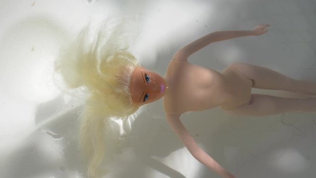 Eerie psycho female doll floats head above clear bathtub water, close up